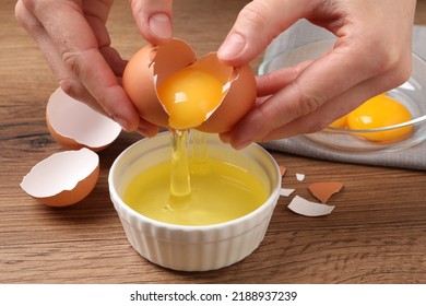 Woman separating egg yolk from white over bowl at wooden table, closeup