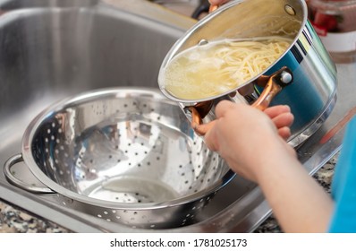 woman separating water from spaghetti with empty silver colander 