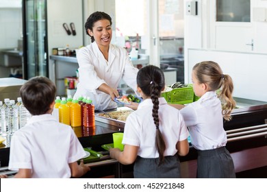 Woman Serving Food To Children In School Canteen