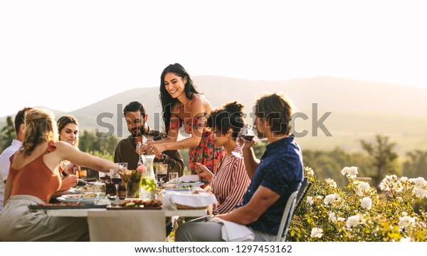 Woman serving food to\
friends at dinner party. Group of young people having a dinner\
together outdoors.