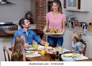 Woman Serving Food To Her Family In The Kitchen At Home