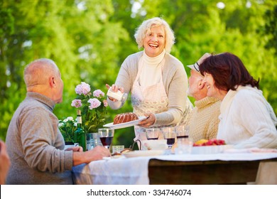 Woman Serving Ring Cake At Birthday Party With Senior People In A Garden