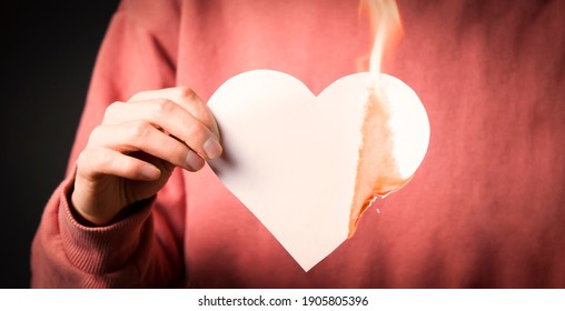 The woman sets the heart on fire, the end of the romantic relationship. Young girl sets fire to a white paper heart, declaring war on inequality in the toxic abusive relationship in which she was. 