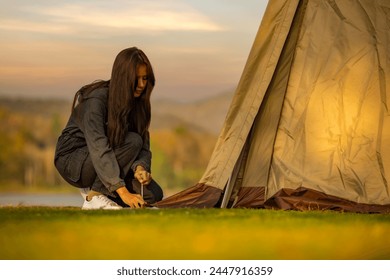 Woman sets up tent during in nature with sunset background. A method of attaching a sling when setting up a tent. Peg anchor in ground with strong fastening tent. Protecting tent from wind and rain. - Powered by Shutterstock