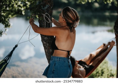 Woman setting up a hammock by a peaceful lakeside, enjoying outdoor adventure, fun, and relaxation on a sunny summer day. - Powered by Shutterstock