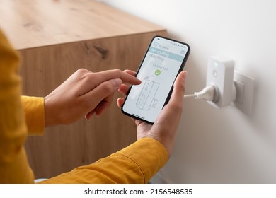 Woman setting a smart plug at home using her smartphone, smart home and domotics concept - Shutterstock ID 2156548535