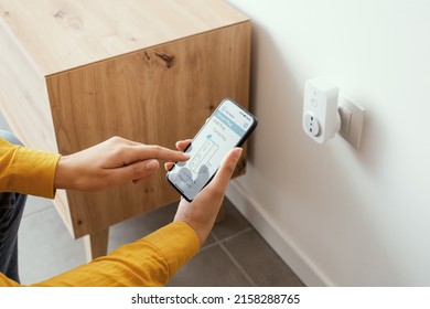 Woman setting a smart plug at home using her smartphone, smart home and domotics concept - Shutterstock ID 2158288765