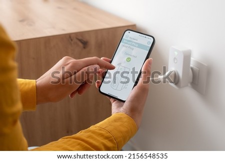 Woman setting a smart plug at home using her smartphone, smart home and domotics concept