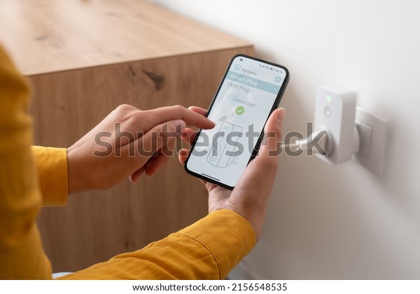 Woman setting a smart plug at home using\
her smartphone, smart home and domotics\
concept