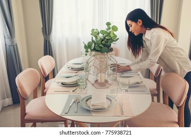 Woman Setting The Table For Dining Room, The Table Is Decorated With Flowers.