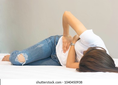 A woman with severe abdominal pain while lying on a bed of white bedroom alone.