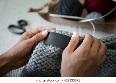 Woman sewing the blank genuine leather label on knitted clothing. Empty tag for your logo. Unrecognizable, closeup, hands only, mockup.