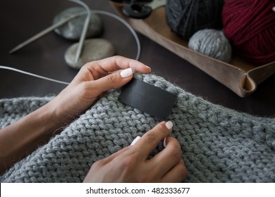 Woman Sewing The Blank Genuine Leather Label On Knitted Clothing. Empty Tag For Your Logo. Unrecognizable, Closeup, Hands Only, Mockup.