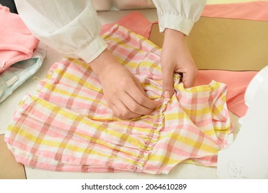 Woman Sewing Children's Clothes On Table