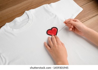 Woman Sewing An Embroidered Heart Patch To A Plain White T-shirt. Embellishment For Casual Clothing, Handcraft Project.