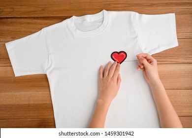 Woman Sewing A Heart Patch On A White T-shirt, Top View. Simple Handcraft Project To Add Fashionable Look To Casual Clothing.