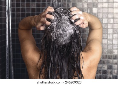 Woman Shampooing Her Long Brown Hair Under A Shower Standing With Her Back To The Camera Working Up A Lather Under The Spray Of Water