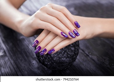 Woman With Shattered Glass Purple Manicure Holds A Ball On Black Wooden Background