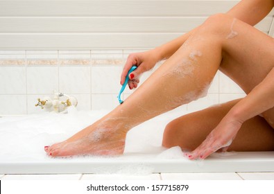 A woman is shaving her legs in the bathroom