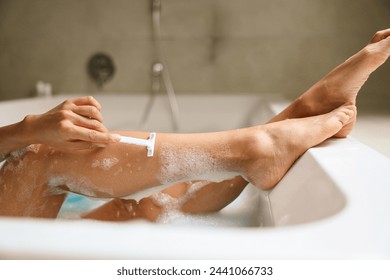 A woman is shaving her legs while enjoying a relaxing bath - Powered by Shutterstock