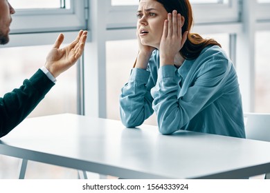 A woman in a shirt sits at a table and looks at a young man who gesticulate with his hands - Shutterstock ID 1564333924