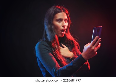 Woman Shocked With The News On Her Phone Screen, Red And Blue Dramatic Image, Strong Expression