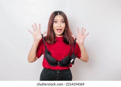A woman is shocked while holding a bra against a white background. Concept of Breast cancer awareness and international no bra day celebration
