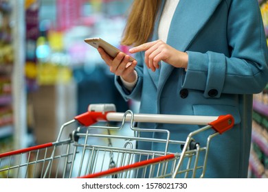 Woman Shopper With Cart In The Shop Aisle With Grocery List On Smartphone During Shopping Food 