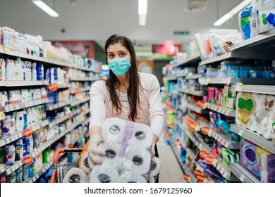 Woman shopper with mask and gloves panic buying and hoarding toilette paper in supply store.Preparing for pathogen virus pandemic quarantine.Prepper buying bulk cleaning supplies due to Covid-19.