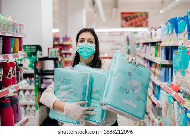 Woman Shopper With Mask And Gloves Panic Buying And Hoarding Disposable Diapers.Preparing For Pathogen Virus Pandemic Quarantine.Prepper Buying Bulk Baby Products Supplies Due To Covid-19.Diapering