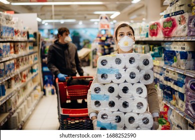 Woman shopper with mask and gloves panic buying and hoarding toilette paper in supply store.Preparing for pathogen virus pandemic quarantine.Prepper buying bulk cleaning supplies due to Covid-19.
