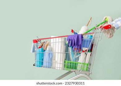 Woman with shopping cart full of cleaning supplies on pale green background - Powered by Shutterstock