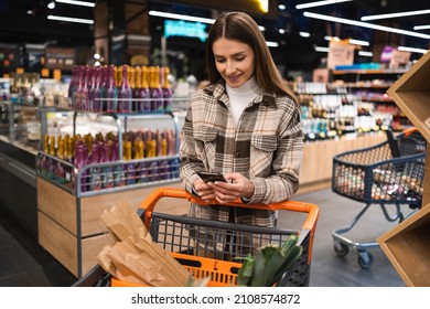 Woman With Shopping Cart In The Supermarket Store Look In Mobile Phone.
Smiling Girl With Smartphone In Grocery Shop
