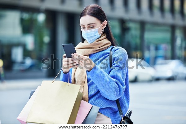 Woman, shopping in covid mask with\
smartphone, communication about sale or discount at retail mall.\
Young shopper in pandemic, bags and contact car service for travel\
and buyer with urban\
background.