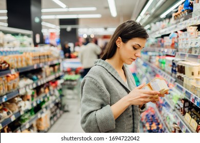 Woman shopping a dairy product in the supermarket grocery store.Reading ingredients,declaration or expiration date before buying it.Nutritional value of the food.Lactose intolerance information