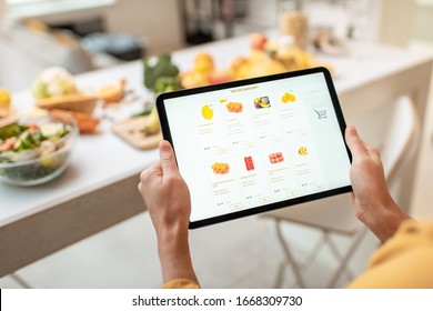 Woman shopping food online using a digital tablet at the kitchen, close-up view on a tablet screen. Concept of buying online using mobile devices