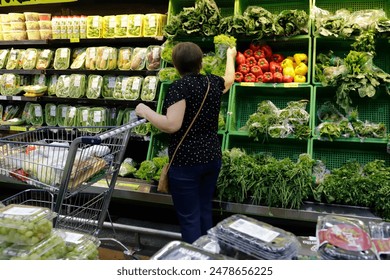 A woman shopping for fresh vegetables in a supermarket, reaching for leafy greens in Brazil - Powered by Shutterstock