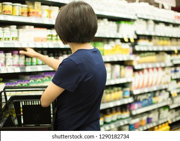 Woman Shopping At Grocery Market Pharmacy. Supermarket Shopper Doing Groceries. Female Holding Basket Trying To Decide Which Products To Buy. Retail Healthcare Medicine, Vitamins, And Supplements.
