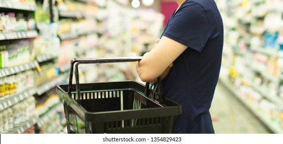 Woman Shopping At Grocery Market Pharmacy. Supermarket Shopper Doing Groceries. Female Holding Basket Trying To Decide Which Products To Buy. Retail Healthcare Medicine, Vitamins, And Supplements.
