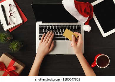 Woman shopping online with credit card and laptop with blank screen. Top view on human hands, keyboard, coffee, Santa hat, Christmas gift on wooden table background. New Year, holiday concept - Powered by Shutterstock