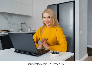 A woman is shopping online from her modern kitchen using a laptop and smartphone - Powered by Shutterstock