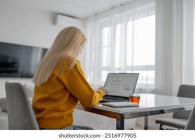 A woman is shopping online from her modern kitchen using a laptop and smartphone - Powered by Shutterstock