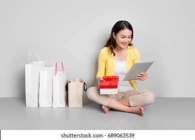 Woman Shopping Online At Home Sitting Besides Row Of Shopping Bags Holding Red Gift Box.