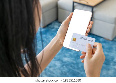 A Woman Shopping Online On Her Sofa At Home With A Smartphone Using A White Credit Card. And Use Your Credit Card To Tap The Screen To Verify The Identity. Concept About Business. Over Shoulder Shot.