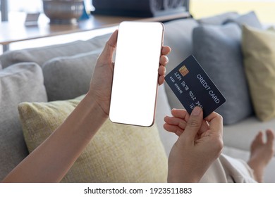 A Woman Shopping Online On Her Sofa At Home With A Smartphone Using A Black Credit Card. And Use Your Credit Card To Tap The Screen To Verify The Identity. Concept About Business. Over Shoulder Shot.