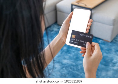 A Woman Shopping Online On Her Sofa At Home With A Smartphone Using A Black Credit Card. And Use Your Credit Card To Tap The Screen To Verify The Identity. Concept About Business. Over Shoulder Shot.