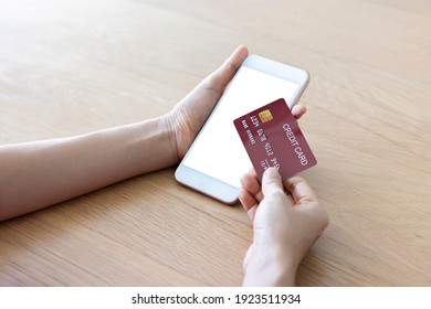 A Woman Shopping Online On Her Table At Home With A Smartphone Using A Red Credit Card. And Use Your Credit Card To Tap The Screen To Verify The Identity. Concept About Business. Over Shoulder Shot.