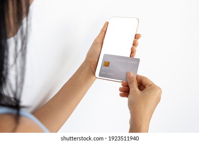 A Woman Shopping Online On Her Sofa At Home With A Smartphone Using A Silver Credit Card. And Use Your Credit Card To Tap The Screen To Verify The Identity. Concept About Business. Over Shoulder Shot.