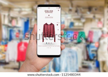 Woman shopping online with smartphone, fashion store in background