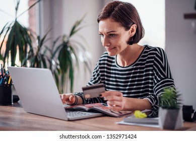 Woman Shopping Online And Using Credit Card While Reading Cosmetic Catalogue
